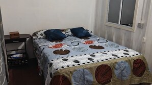 Quarto com cama, janela e uma pequena mesa com uma caixa.