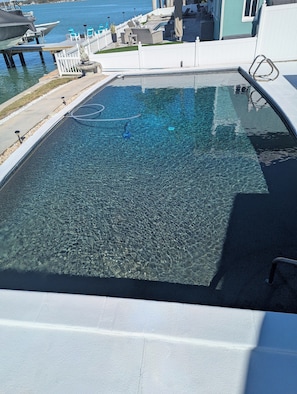 Une piscine aux eaux cristallines offrant une vue sur la mer, une clôture blanche et des chaises longues.