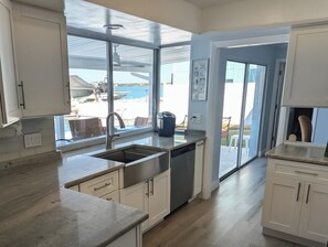 A modern kitchen with a large window, a built-in dishwasher, and a view of the beach. - Treasure Island Beach Waterfront Pool and Dock Home (Treasure Island)