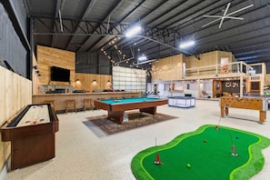 An indoor recreational area with a pool table, foosball table, and a mini-golf setup.