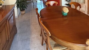 A dining area with a wooden table and chairs, a kitchen with cabinets, and a living room with a sofa and a door.