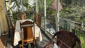 A conservatory with a table and chairs, a glass railing, and a view of trees and shrubs. - Charming house in Le Faou, a "little town of character", between land and sea. (Le Faou)