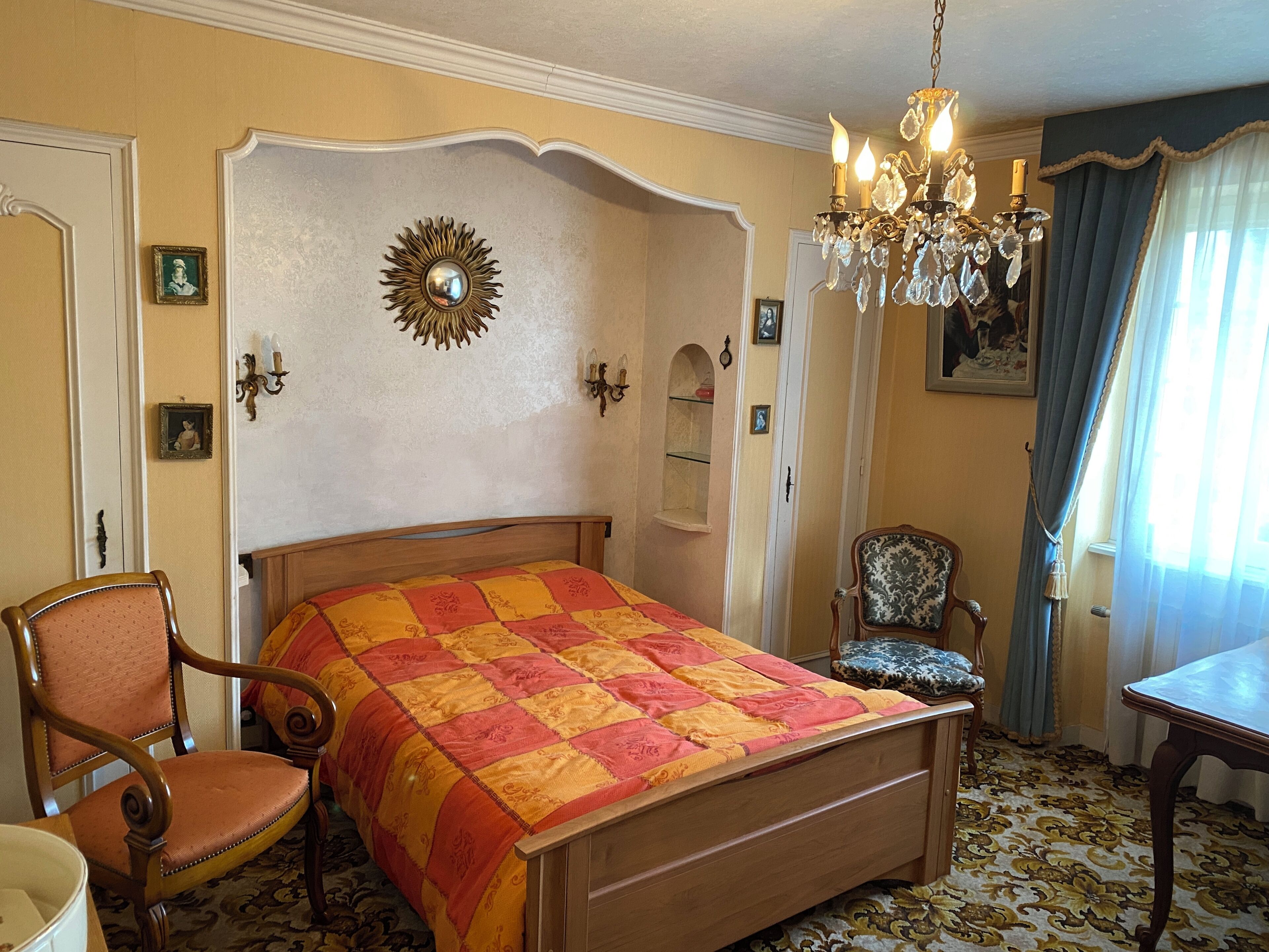 A bedroom with a wooden bed, a chandelier, a chair, and a table.