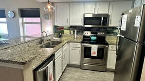 Una cocina moderna con armarios blancos, electrodomésticos de acero inoxidable, encimera de granito y tragaluz.
