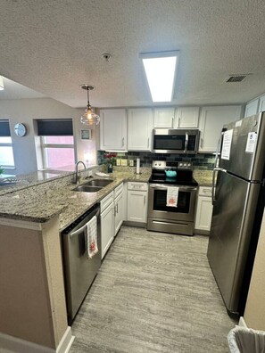 A modern kitchen with white cabinets, stainless steel appliances, a granite countertop, and a skylight. - Sunny Shores Oceanview Condo (Myrtle Beach)