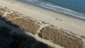 Una playa con cielo despejado, mar tranquilo y un camino de arena que lleva a la orilla.
