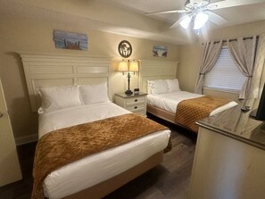 A hotel room with two beds, a nightstand with a lamp, a ceiling fan, and artwork on the walls. - Oasis By The Lazy River (Myrtle Beach)