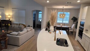 Ett modernt vardagsrum med en soffa, ett soffbord och en köksdel med en vit bänkskiva och diskho.