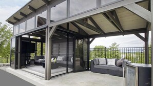 Un espacio al aire libre techado con sofá y sillones, una parrilla y vistas al paisaje.