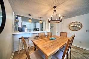 Ein Essbereich mit Holztisch, sechs Stühlen, einer Chandelierleuchtre und einer Küche im Hintergrund.
