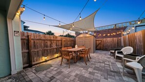 Eine Terrasse mit Holztisch und -stühlen, einem Schuppen und Lichterketten.