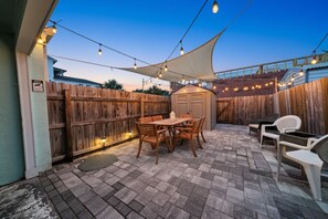 Eine Terrasse mit Holztisch und -stühlen, einem Schuppen und Lichterketten.