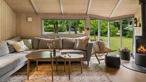 Een gezellige woonkamer met een bank, twee ronde tafels, een open haard en uitzicht op de omgeving.