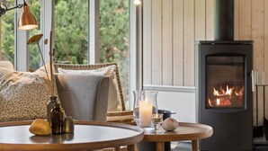 Een gezellige woonkamer met een open haard, een bank, een ronde houten tafel en een lamp.