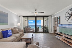 Ett vardagsrum med en soffa, ett soffbord, en tv och en balkong med utsikt över havet.
