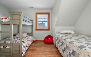 Une chambre de dortoir avec des lits superposés, une fenêtre, un pouf rouge et une couvre-lit à motifs.