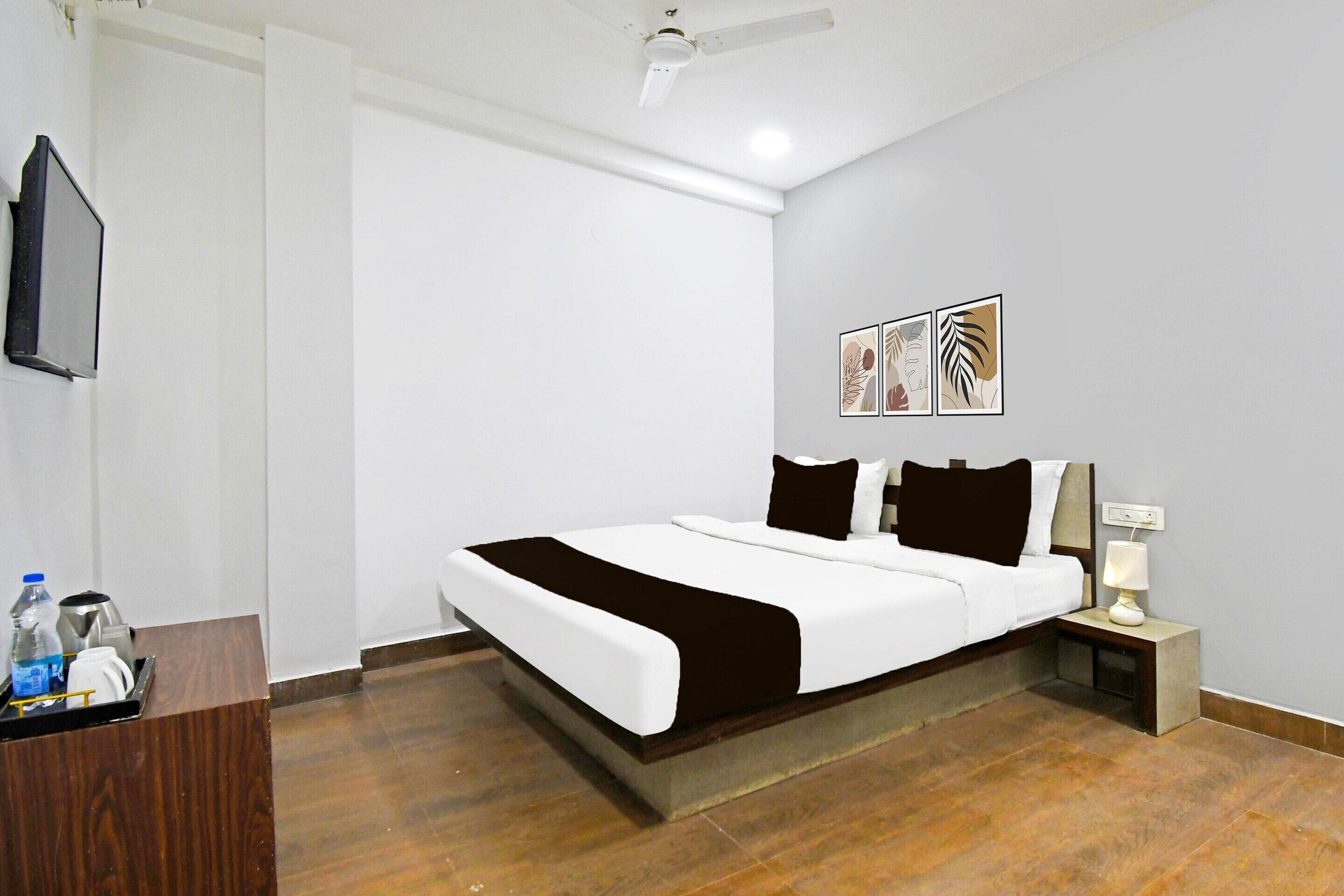 A hotel room with a bed, bedside table, lamp, artwork, and a television.