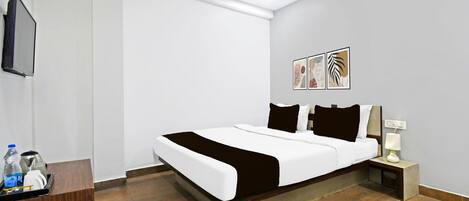 A hotel room with a bed, bedside table, lamp, artwork, and a television.