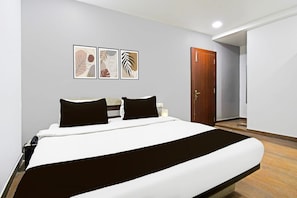 A hotel room with a bed, a wooden door, and three framed wall art pieces. - Deluxehotel Kamla Inn 2 (Bhubaneshwar)