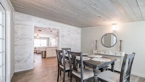 A dining area with a wooden table and chairs, a white marble wall, and a kitchen in the background. - Beautiful Tampa Pool/Hot Tub Home-Spacious Yard (Tampa)