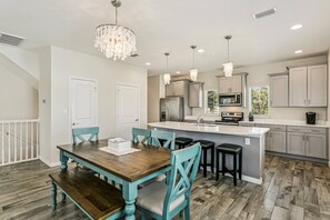 A modern kitchen with a central island, grey cabinets, and a dining area with a wooden table and blue chairs. - New Listing! Lost Key| Private Beach Club| Two pools| Tennis/Pickleball| Free Golf and Activities (Pensacola)