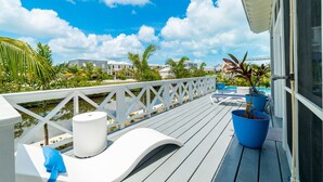 Una terraza de madera con barandilla, mobiliario exterior y plantas en macetas.