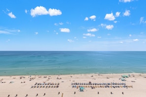 Une plage bordée de rangées de transats et de parasols, un ciel dégagé et une mer calme.