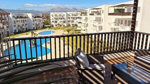Un balcon donnant sur une piscine, un espace détente avec un canapé et une table, et une structure en forme de pergola.