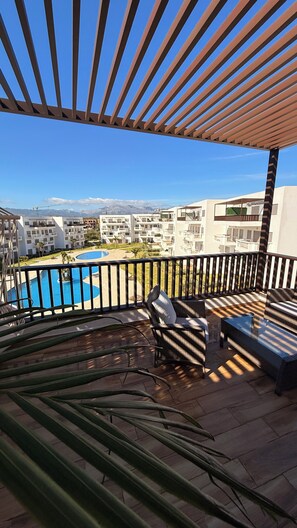 Ein Balkon mit Blick auf einen Swimmingpool, eine Lounge mit Sofa und Tisch sowie eine Pergola.