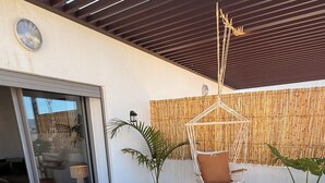 Une terrasse avec un canapé en osier, des plantes en pot et un mur en bambou.