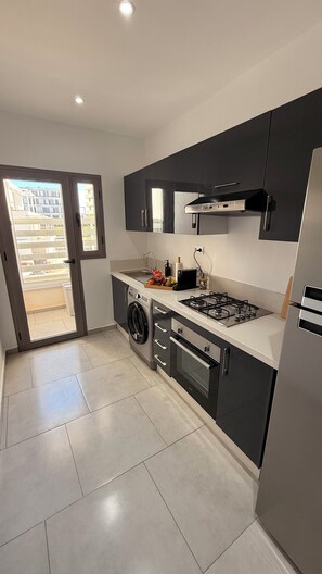 Eine moderne Küche mit Gaskochfeld, Backofen, Waschmaschine und einem großen Fenster.