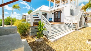 Un edificio moderno blanco con terraza de madera, una escalera y zona de piscina.