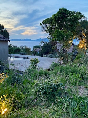 Un jardin avec une terrasse en bois, un grand arbre et une vue sur la mer.