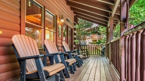A wooden porch with Adirondack chairs, a railing, and a view of a forested area. - 1/2 Mile to Parkway*3 BR*Hot Tub*Games*Comm. Pool (Pigeon Forge)