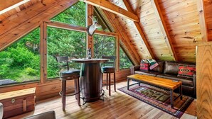 A wooden interior with a dining table, chairs, a sofa, and a large window overlooking greenery. - 1/2 Mile to Parkway*3 BR*Hot Tub*Games*Comm. Pool (Pigeon Forge)