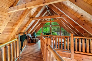 Ein Dachzimmer aus Holz mit Holzbalkon, einer Couch und einem kleinen Tisch.