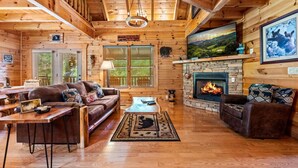 A log cabin interior with a fireplace, wooden walls, a sofa, and a dining area. - 1/2 Mile to Parkway*3 BR*Hot Tub*Games*Comm. Pool (Pigeon Forge)