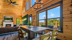 A wooden interior with a dining area, seating, a fireplace, and large windows. - New! Indoor Pool w/Hot Tub*Putting Green*Pets! (Sevierville)
