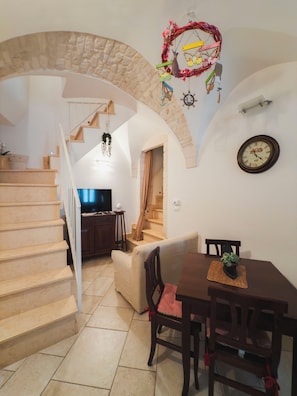 A staircase leading to a living area with a TV, a dining table with chairs, and a clock on the wall. - Barocco Art House - Elegant apartment with terrace in Martina Franca (Martina Franca)
