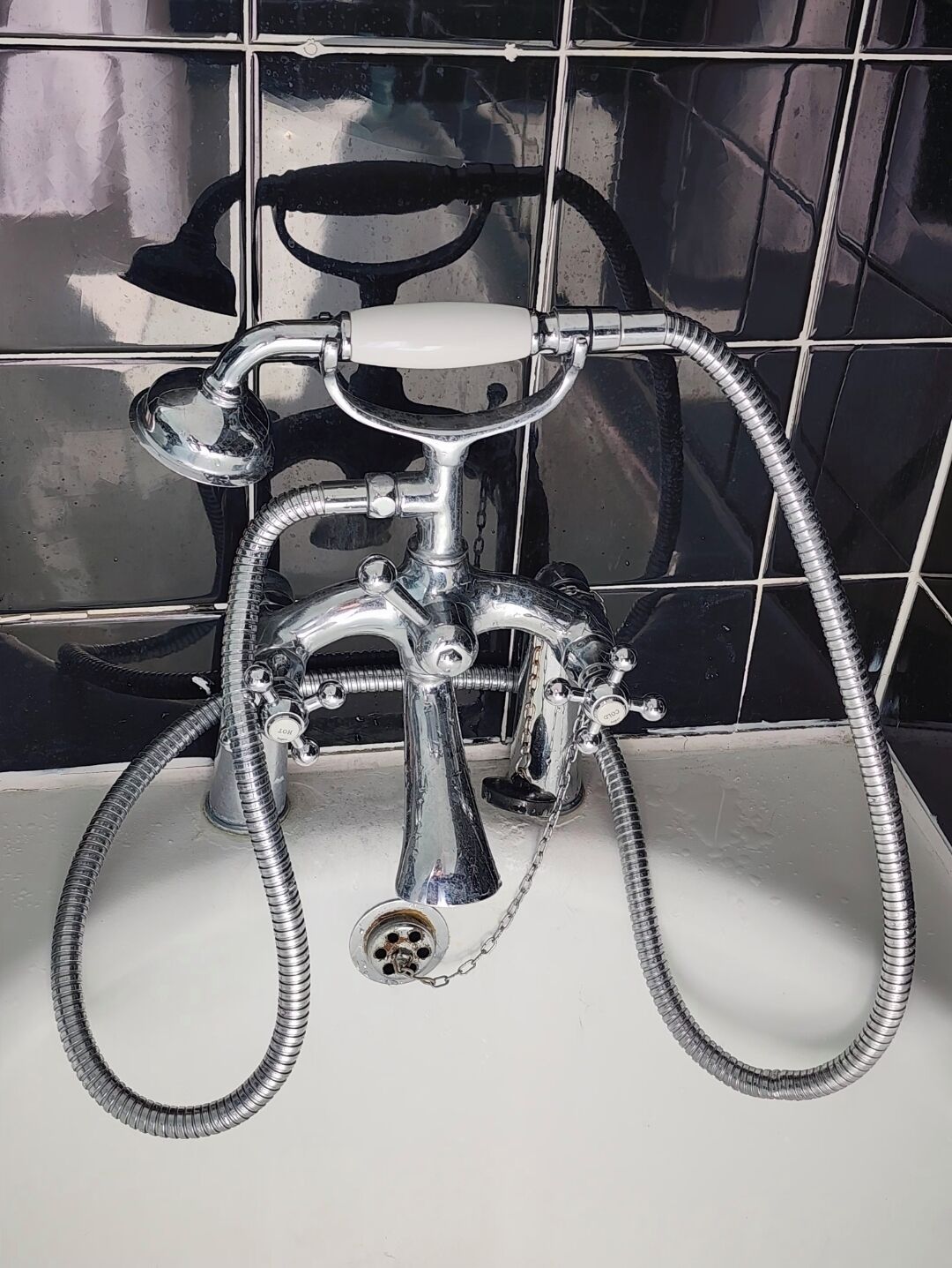 A bathroom with a chrome faucet, a showerhead, and a flexible hose.