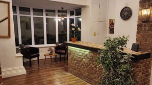 Una habitación con suelo de madera, una pared decorativa de ladrillo, un mostrador de recepción, una planta en maceta y un ventanal grande.