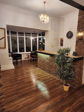 A room with a wooden floor, a brick accent wall, a reception desk, a potted plant, and a large window.