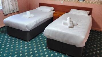 Una habitación de hotel con dos camas, cabecera de madera, alfombra estampada y cortina con motivos florales.