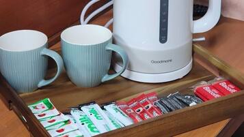 A white electric kettle, two light blue mugs, and a tray with tea and biscuit packets.
