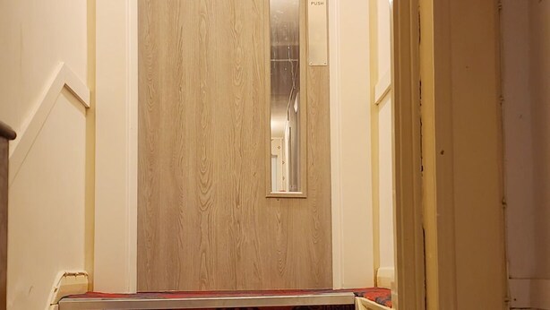 Una puerta de madera con un botón pulsador, un espejo y un letrero encima.