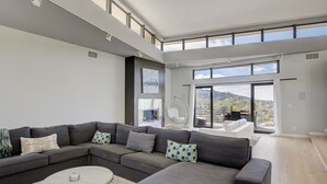 A modern living room with a sectional sofa, a round coffee table, and large windows offering a city view. - The Hollywood Hills Executive - Incredible Sunsets- Next to Studios! (Los Angeles)