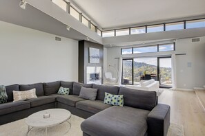 A modern living room with a sectional sofa, a round coffee table, and large windows offering a city view. - The Hollywood Hills Executive - Incredible Sunsets- Next to Studios! (Los Angeles)