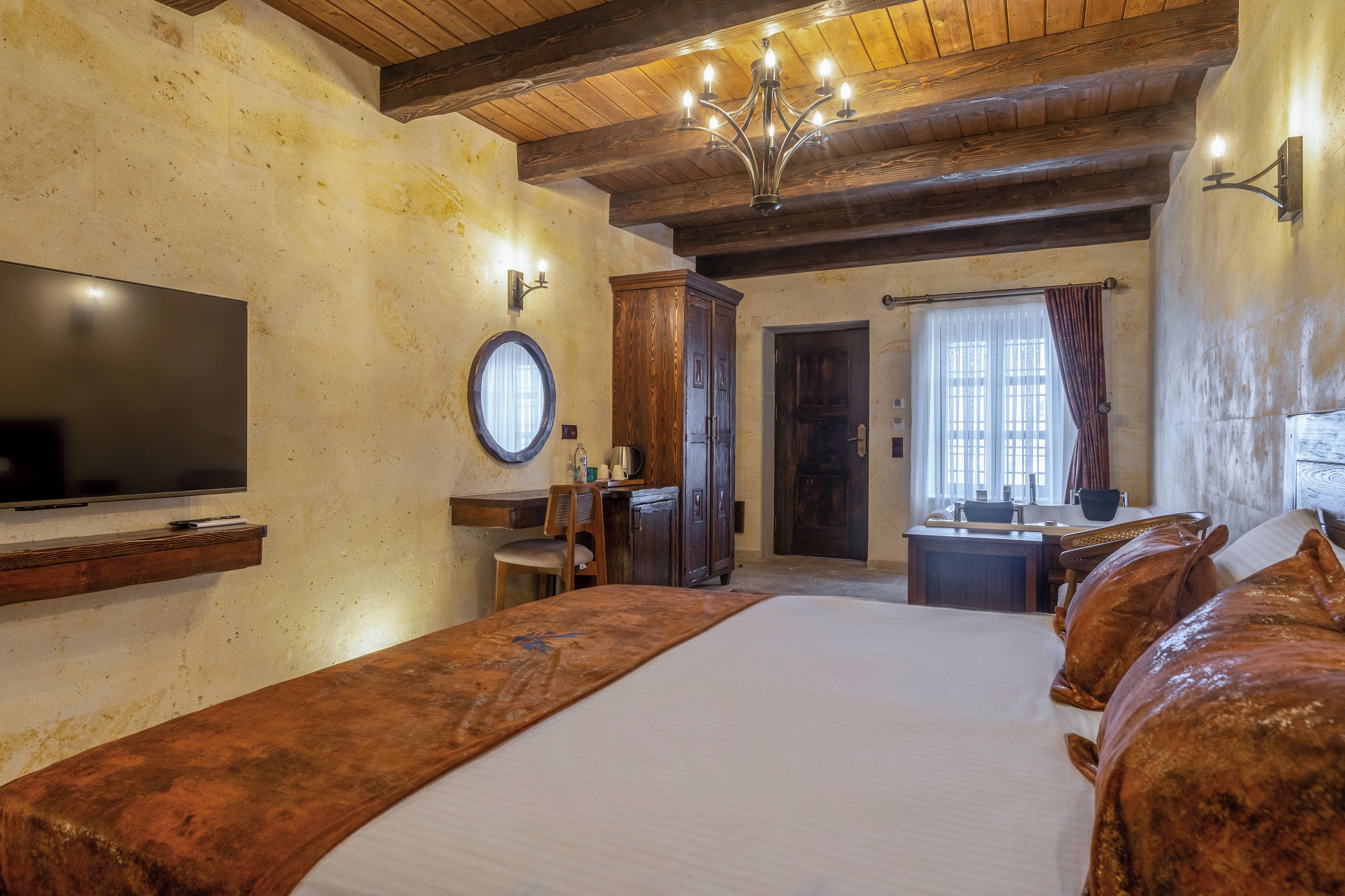 A hotel room with a large bed, a television, a wooden ceiling, and a window with curtains.