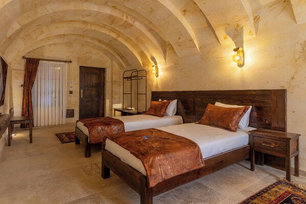 A hotel room with two beds, a wooden headboard, a nightstand, a bench, and a patterned rug. - Noble Blue Cappadocia (Urgup)