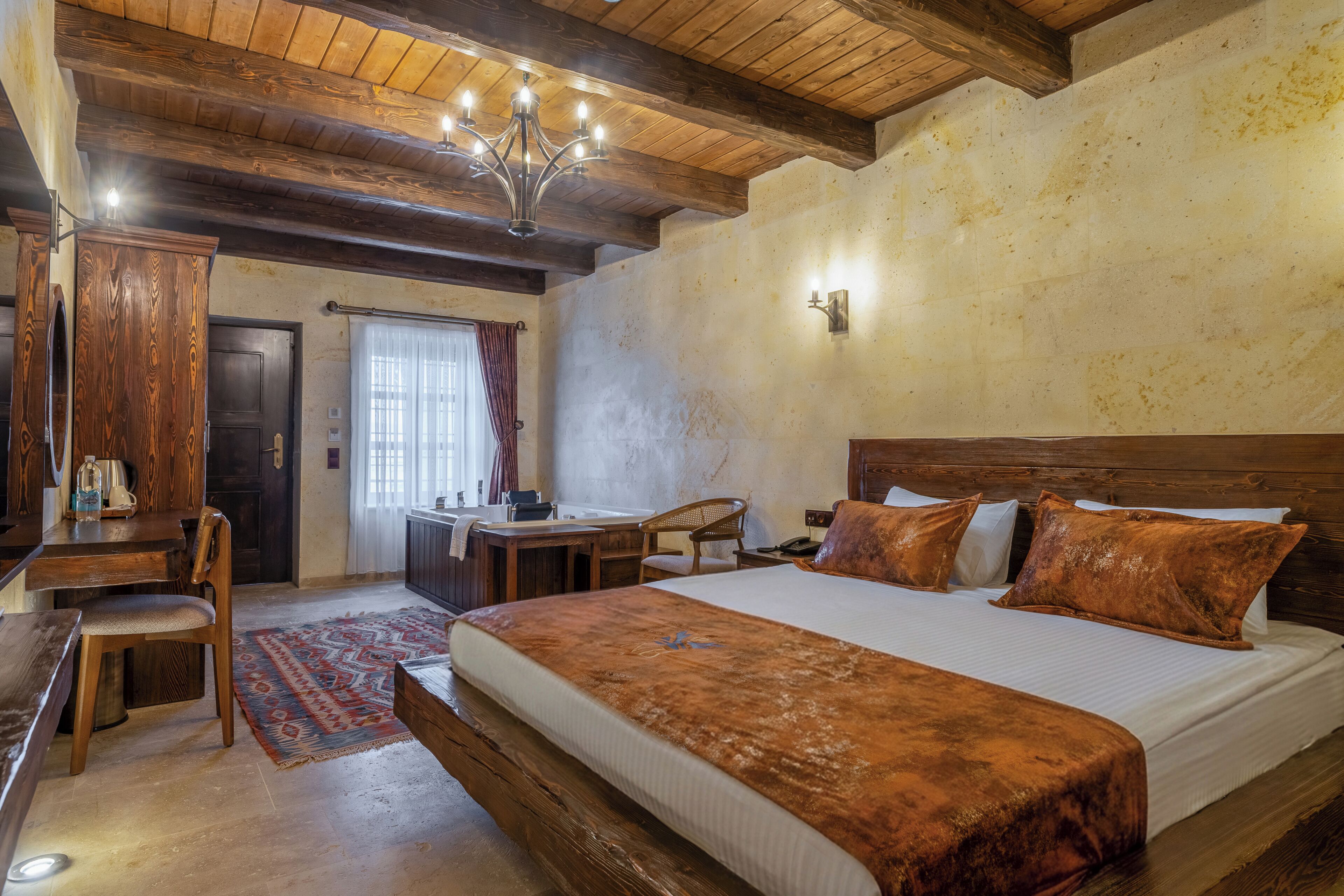 A bedroom with a wooden ceiling, a large bed with pillows, a desk, and a chair.